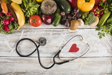 Frontend elevated view stethoscope with heart shape near fresh vegetables wooden desk