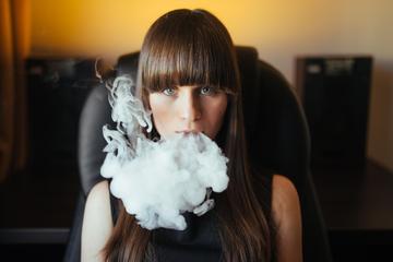 Frontend young beautiful girl exhaling smoke from hookah looking camera